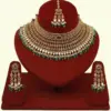 Premium matte gold bridal necklace set with ruby and green stones, heavy choker design, hanging green beads, matching earrings and maang tikka displayed on red stand, Ishwar Arts and Crafts