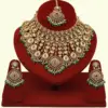 Traditional matte gold necklace set with ruby stones, green beads, intricate carvings, earrings, and maang tikka displayed on red stand, Ishwar Arts and Crafts