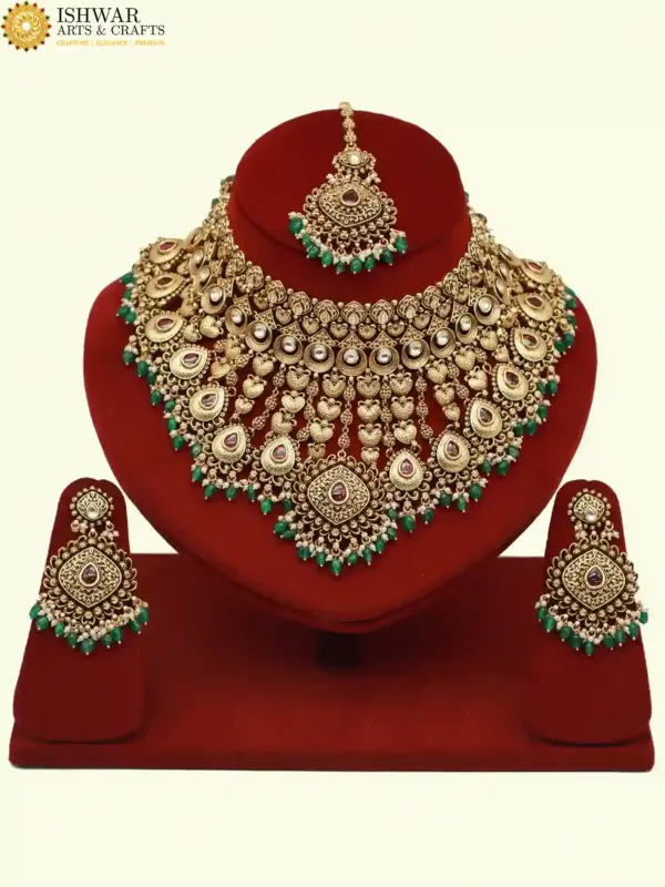 Traditional matte gold necklace set with ruby stones, green beads, intricate carvings, earrings, and maang tikka displayed on red stand, Ishwar Arts and Crafts
