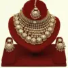 Heavy matte gold brass bridal necklace set with kundan stones, earrings, and maang tikka displayed on red jewelry stand, Ishwar Arts and Crafts