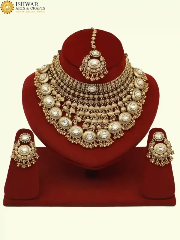 Heavy matte gold brass bridal necklace set with kundan stones, earrings, and maang tikka displayed on red jewelry stand, Ishwar Arts and Crafts