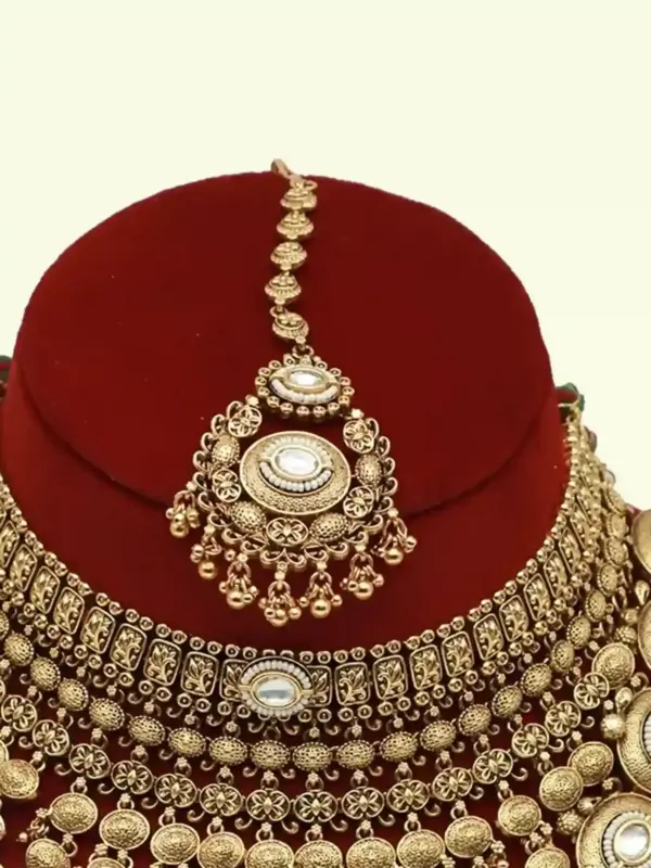 Heavy matte gold brass bridal necklace set with kundan stones, earrings, and maang tikka displayed on red jewelry stand, Ishwar Arts and Crafts