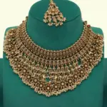 Antique gold intricate carving bridal necklace set with matching heavy earrings and maang tikka displayed on green jewelry stand, Ishwar Arts and Crafts