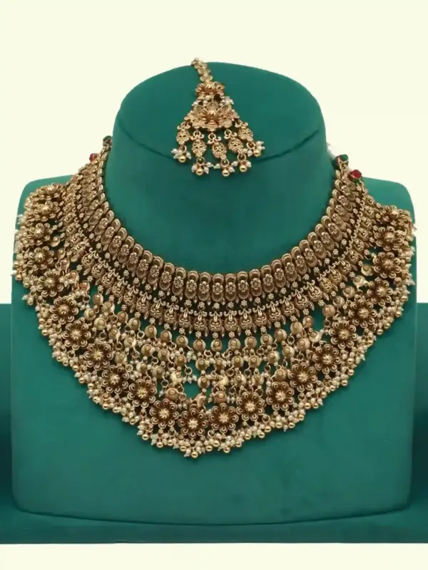 Antique gold intricate carving bridal necklace set with matching heavy earrings and maang tikka displayed on green jewelry stand, Ishwar Arts and Crafts