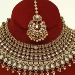 Antique gold brass bridal necklace set with Kundan stones, matching earrings, and maangtika on red display, Ishwar Arts and Crafts