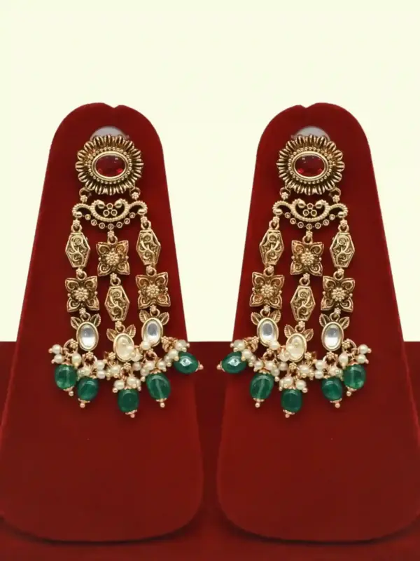Premium matte gold bridal necklace set with ruby and green stones, heavy choker design, hanging green beads, matching earrings and maang tikka displayed on red stand, Ishwar Arts and Crafts