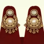 Heavy matte gold brass bridal necklace set with kundan stones, earrings, and maang tikka displayed on red jewelry stand, Ishwar Arts and Crafts