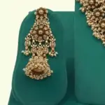 Antique gold intricate carving bridal necklace set with matching heavy earrings and maang tikka displayed on green jewelry stand, Ishwar Arts and Crafts