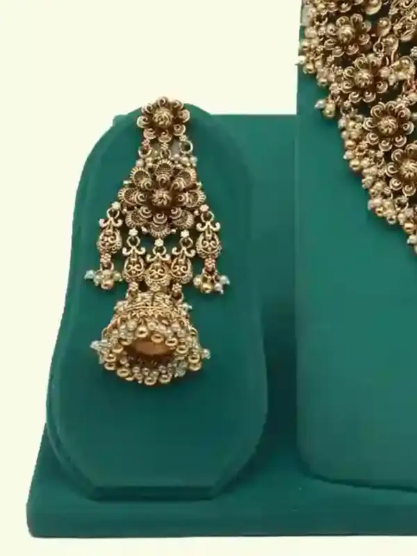 Antique gold intricate carving bridal necklace set with matching heavy earrings and maang tikka displayed on green jewelry stand, Ishwar Arts and Crafts