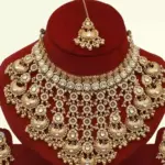 Antique gold bridal necklace set with hanging beads, matching jhumka earrings, and maangtika on red display stand, Ishwar Arts and Crafts