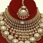 Heavy matte gold brass bridal necklace set with kundan stones, earrings, and maang tikka displayed on red jewelry stand, Ishwar Arts and Crafts