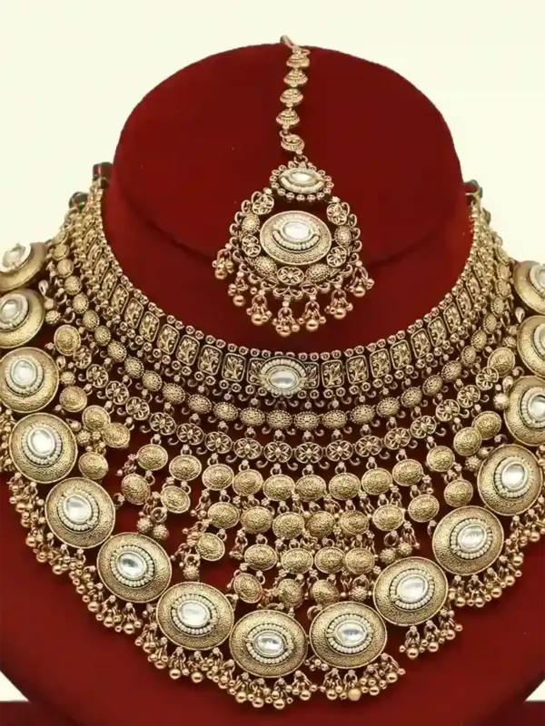 Heavy matte gold brass bridal necklace set with kundan stones, earrings, and maang tikka displayed on red jewelry stand, Ishwar Arts and Crafts