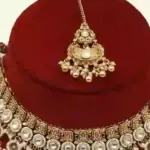 Antique gold bridal necklace set with hanging beads, matching jhumka earrings, and maangtika on red display stand, Ishwar Arts and Crafts