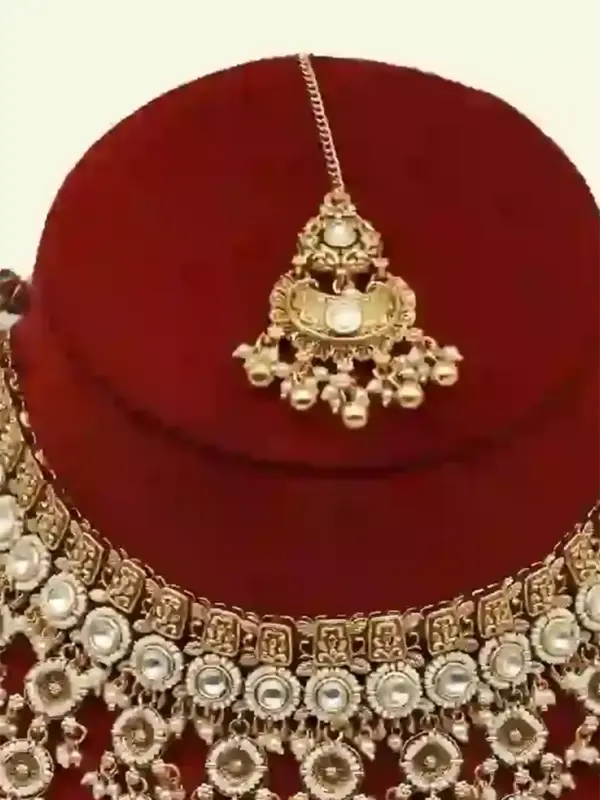 Antique gold bridal necklace set with hanging beads, matching jhumka earrings, and maangtika on red display stand, Ishwar Arts and Crafts