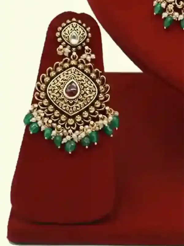 Traditional matte gold necklace set with ruby stones, green beads, intricate carvings, earrings, and maang tikka displayed on red stand, Ishwar Arts and Crafts