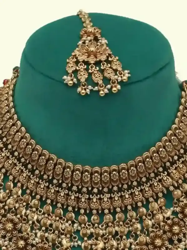 Antique gold intricate carving bridal necklace set with matching heavy earrings and maang tikka displayed on green jewelry stand, Ishwar Arts and Crafts