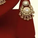 Heavy matte gold brass bridal necklace set with kundan stones, earrings, and maang tikka displayed on red jewelry stand, Ishwar Arts and Crafts