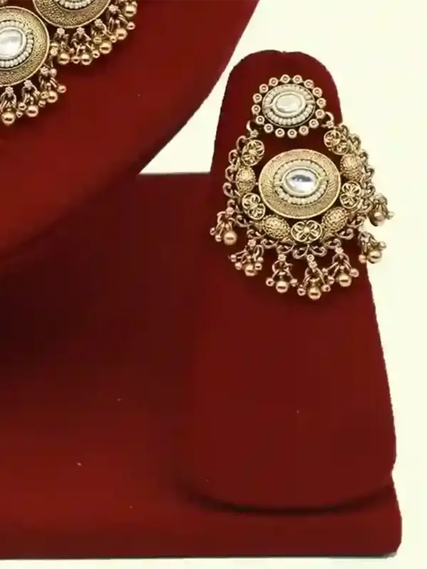Heavy matte gold brass bridal necklace set with kundan stones, earrings, and maang tikka displayed on red jewelry stand, Ishwar Arts and Crafts